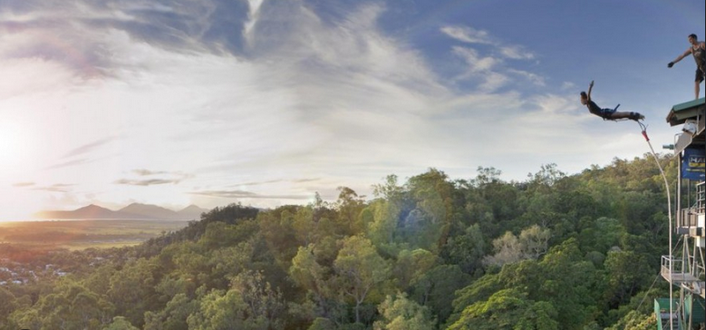 Bungee jumper leaping from a tower above forested hills at golden hour